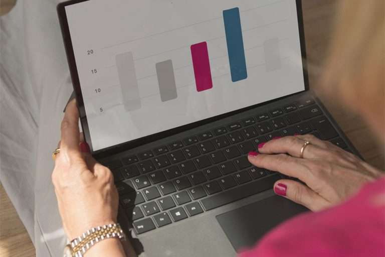 Steuerblog für Selbstständige: Businessplanung. Barbara Kutzka sitzt am Boden mit einem Laptop auf dem Schoß. Der Bildschirm zeigt ein Balkendiagramm.