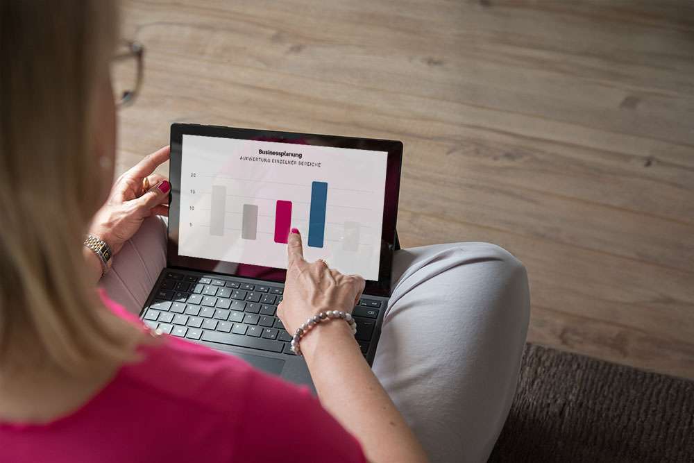 Headerbild 10 Schritte zur Businessplanung: Barbara Hülsmann sitzt auf dem Boden mit Laptop auf dem Schoss und zeigt auf den Bildschirm, der ein Balkendiagramm zeigt.