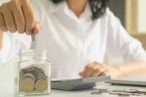 Headerbild Einkommensteuer-Vorauszahlung anpassen. Frau wirft Geldmünzen in ein Sparglas.