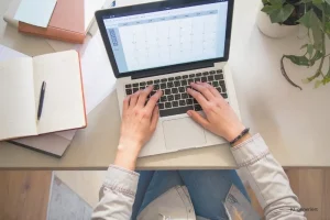 Headerbild Steuerglossar Zusammenfassende Meldung. Eine Frau sitzt am Laptop am Tisch. Auf dem Laptop ist ein Kalender zu sehen.