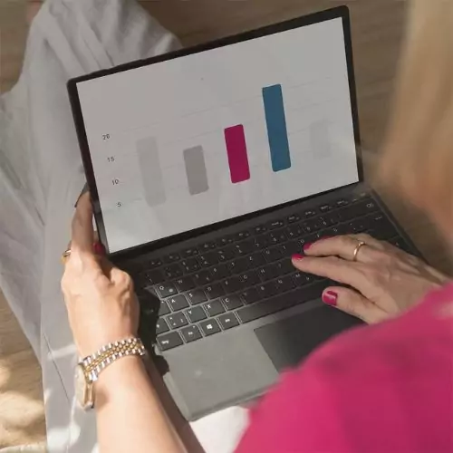 Kleinunternehmerwissen TaxLounge Consulting. Barbara sitzt an Laptop. Auf dem Laptop ist ein Balkendiagramm zu sehen.