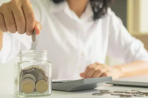 Headerbild Einkommensteuer-Vorauszahlung anpassen. Frau wirft Geldmünzen in ein Sparglas.